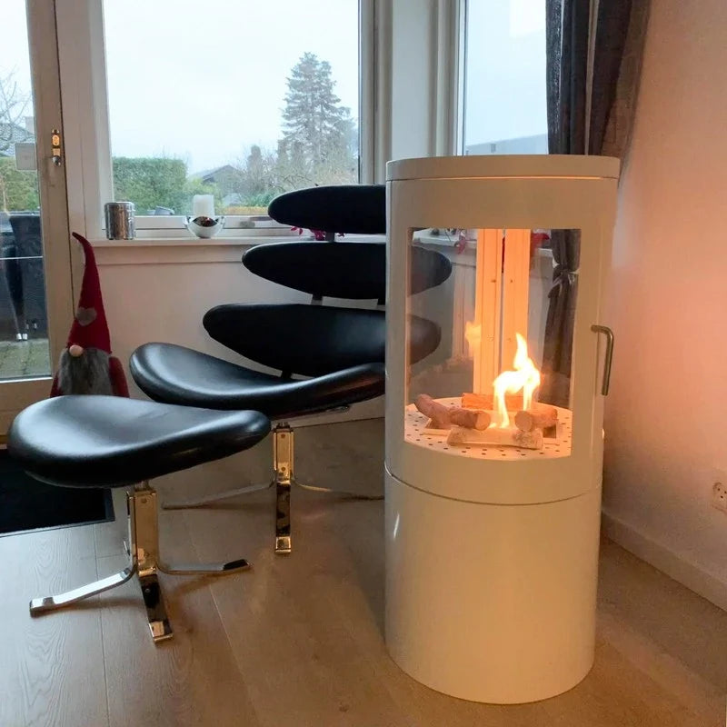 Columbus White Bioethanol Stove with 360-View lit in a real customer's living room with a black leather chair